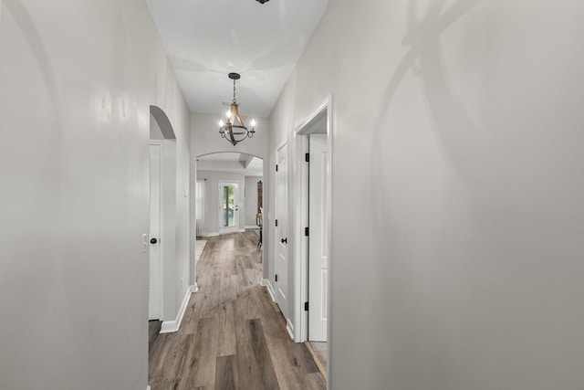 hall with arched walkways, baseboards, and wood finished floors