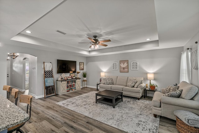 living area with a tray ceiling, ceiling fan, baseboards, and visible vents