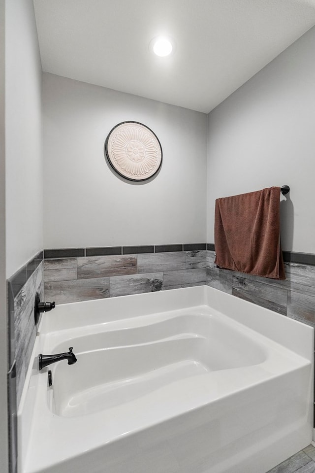 full bath featuring tile walls, a garden tub, recessed lighting, and a wainscoted wall