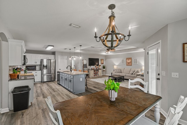 dining area featuring light wood-type flooring, visible vents, baseboards, and ceiling fan with notable chandelier