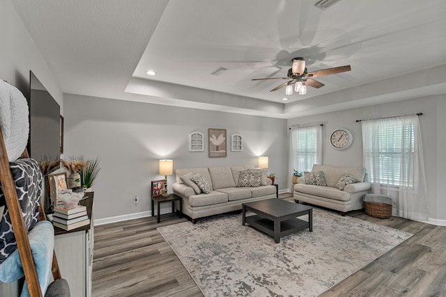 living area featuring baseboards, visible vents, ceiling fan, and wood finished floors