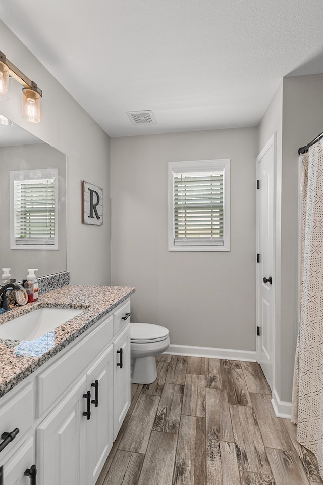bathroom with toilet, baseboards, visible vents, vanity, and wood finished floors