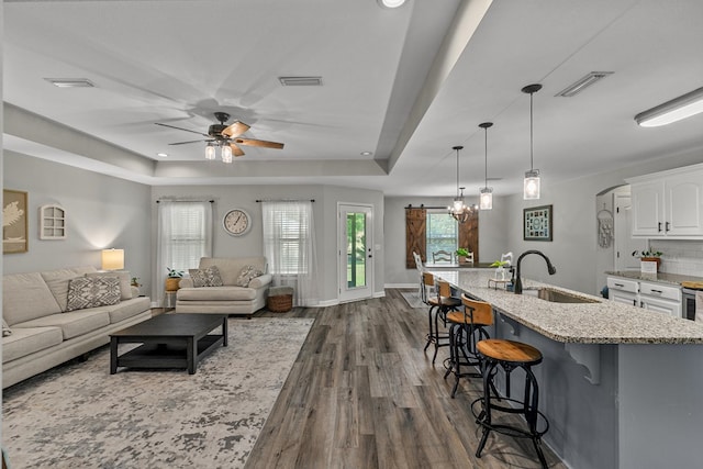 living area featuring dark wood finished floors, a tray ceiling, visible vents, and ceiling fan with notable chandelier