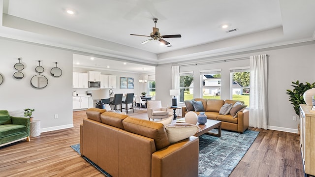 living room with ceiling fan, light hardwood / wood-style floors, crown molding, and a tray ceiling