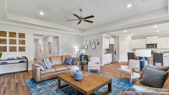 living room featuring a raised ceiling, crown molding, ceiling fan, and dark wood-type flooring