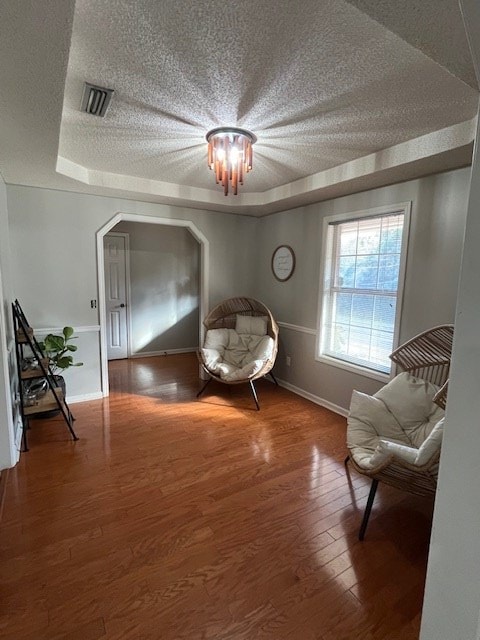 living area with a textured ceiling, a tray ceiling, and dark hardwood / wood-style floors