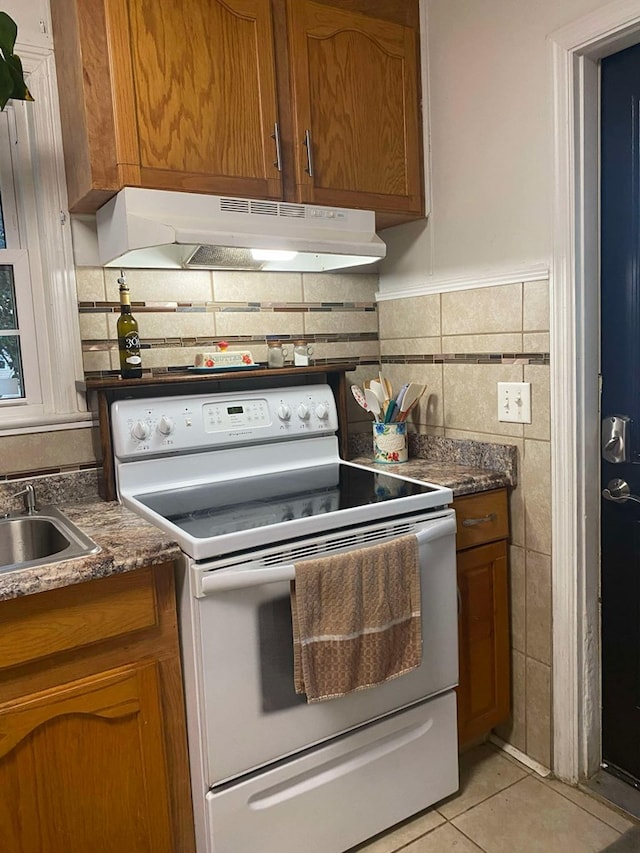 kitchen with electric range, brown cabinets, under cabinet range hood, tile walls, and light tile patterned flooring