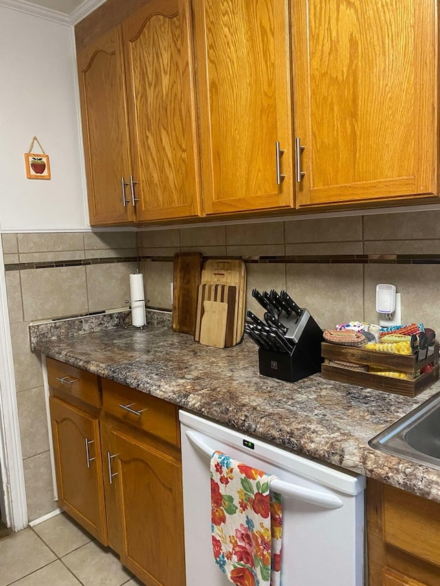 kitchen with light tile patterned floors, dark stone countertops, brown cabinetry, and white dishwasher