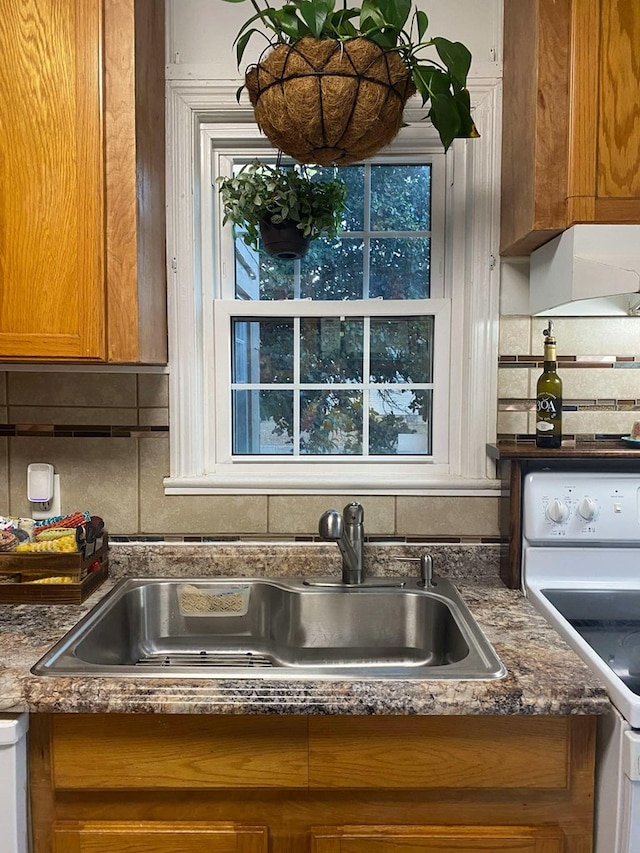 kitchen with white electric stove, decorative backsplash, brown cabinetry, and a sink