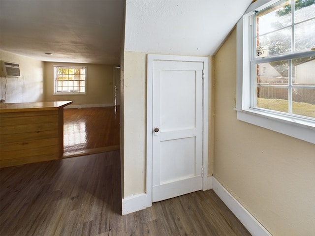 corridor with lofted ceiling, a wall mounted AC, and dark wood-type flooring