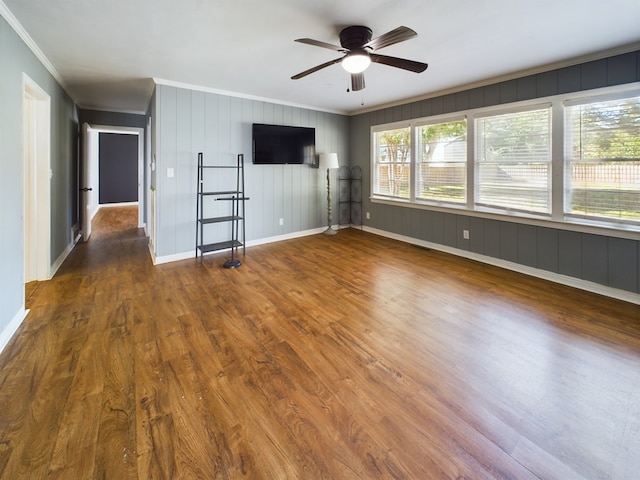 unfurnished living room with crown molding, ceiling fan, dark wood-type flooring, and wood walls