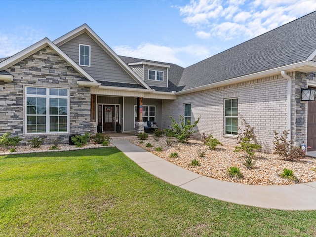view of front of house with roof with shingles, covered porch, stone siding, and a front yard