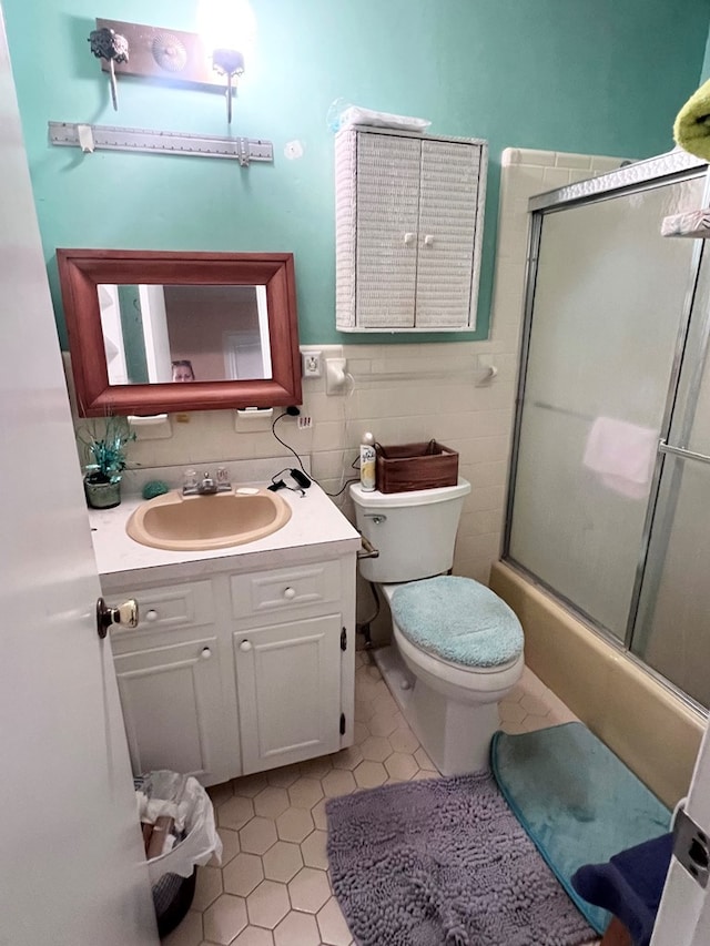 full bathroom featuring combined bath / shower with glass door, tile patterned floors, vanity, tile walls, and toilet