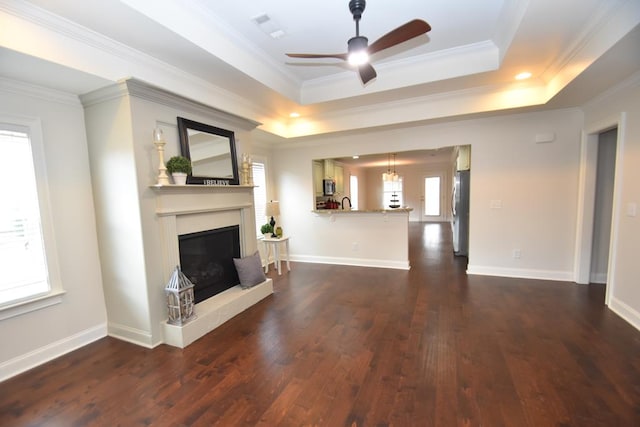 unfurnished living room featuring a tray ceiling, ceiling fan, dark wood-type flooring, and crown molding