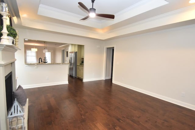 unfurnished living room with sink, ceiling fan, crown molding, dark wood-type flooring, and a raised ceiling