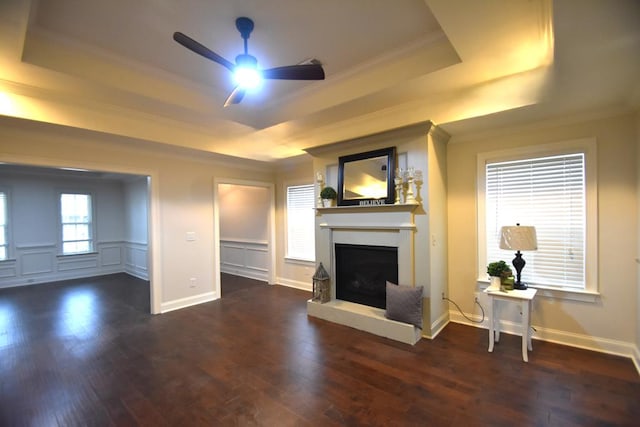 unfurnished living room with a tray ceiling, dark wood-type flooring, ornamental molding, and ceiling fan