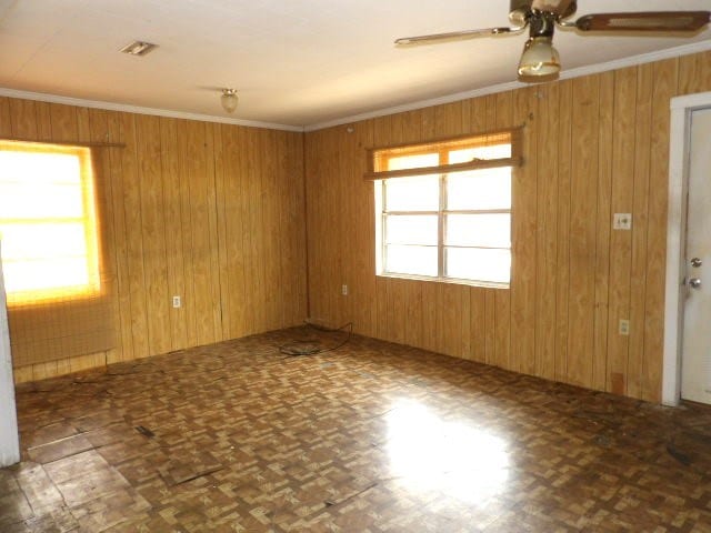 unfurnished room featuring wooden walls, a ceiling fan, and ornamental molding