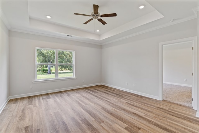 empty room featuring ceiling fan, light wood-type flooring, ornamental molding, and a tray ceiling