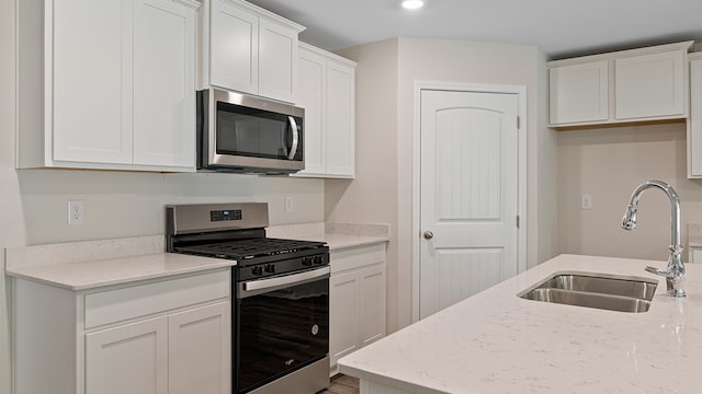 kitchen with light stone countertops, appliances with stainless steel finishes, white cabinetry, and sink