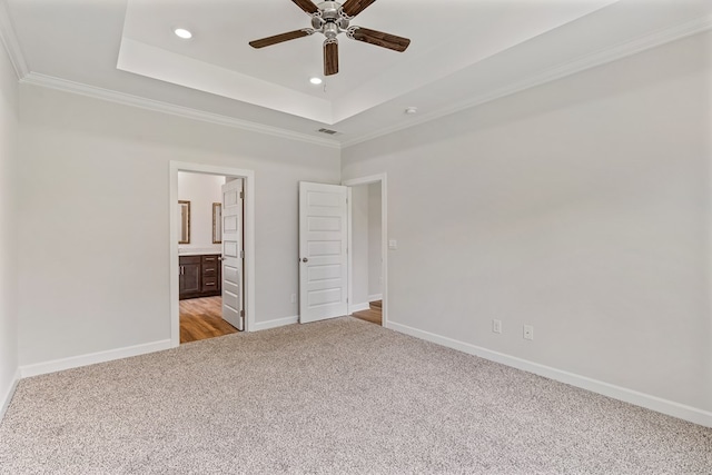 unfurnished bedroom with light carpet, crown molding, ceiling fan, connected bathroom, and a tray ceiling