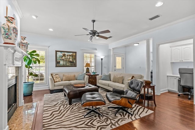 living area featuring a ceiling fan, visible vents, a high end fireplace, dark wood-style floors, and ornamental molding