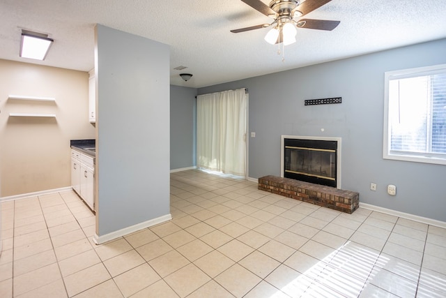 unfurnished living room featuring ceiling fan, light tile patterned floors, a textured ceiling, and a brick fireplace