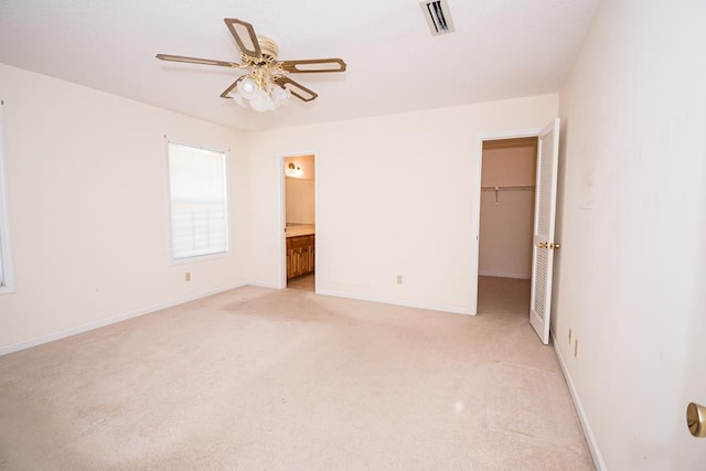 unfurnished bedroom with light colored carpet, visible vents, baseboards, a closet, and a walk in closet