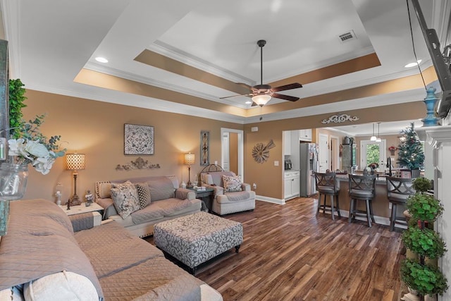 living room featuring dark hardwood / wood-style floors, ceiling fan, a raised ceiling, and ornamental molding