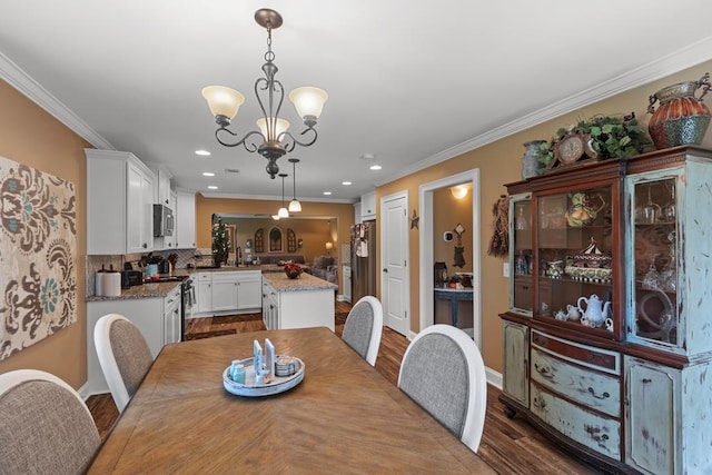 dining room featuring a notable chandelier, sink, dark wood-type flooring, and crown molding