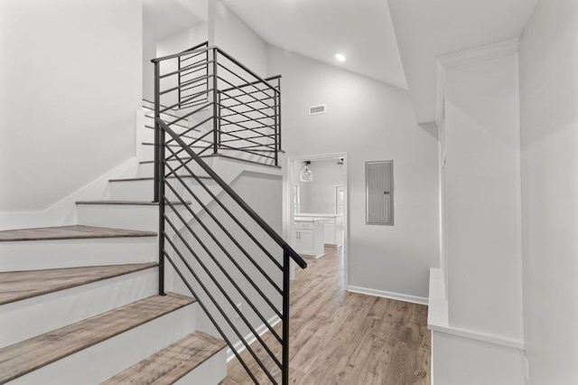 stairs with electric panel, lofted ceiling, and hardwood / wood-style flooring