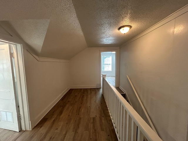 hall with dark hardwood / wood-style flooring, a textured ceiling, and vaulted ceiling