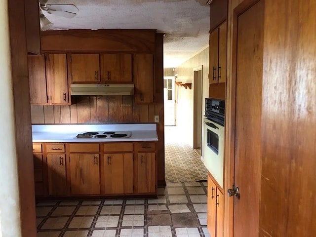 5131 County Rd 417, Kinston, AL 36453 - kitchen with under cabinet range hood, cooktop, white oven, light floors, and brown cabinetry