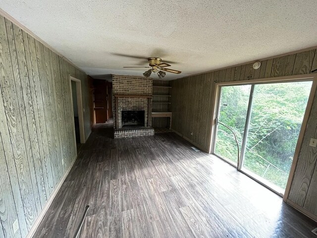 5131 County Rd 417, Kinston, AL 36453 - unfurnished living room featuring wooden walls, a ceiling fan, a textured ceiling, wood finished floors, and a fireplace