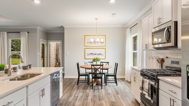 kitchen featuring white cabinets, sink, decorative light fixtures, light hardwood / wood-style floors, and stainless steel appliances