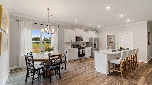 kitchen with a breakfast bar, a kitchen island with sink, an inviting chandelier, white cabinetry, and stainless steel appliances