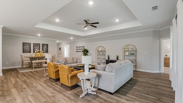 living room with a raised ceiling, ceiling fan, hardwood / wood-style floors, and ornamental molding