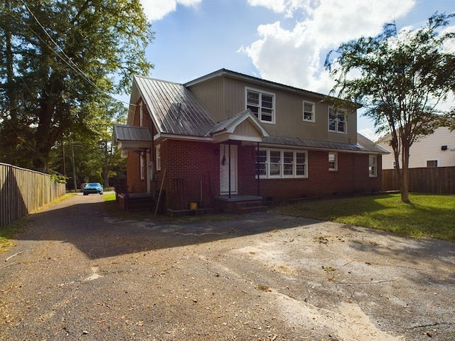 view of front facade featuring metal roof, brick siding, and fence