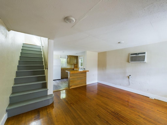 staircase with baseboards, a wall unit AC, hardwood / wood-style floors, and a textured ceiling