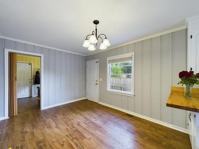unfurnished dining area featuring visible vents, wood finished floors, an inviting chandelier, and crown molding