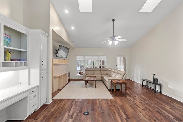 living room featuring built in desk, ceiling fan, vaulted ceiling with skylight, dark hardwood / wood-style floors, and built in shelves