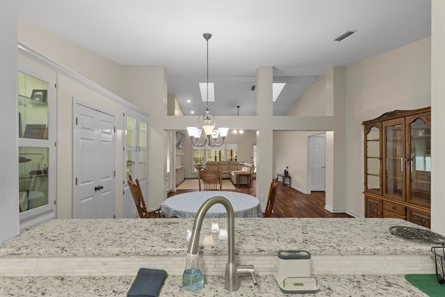 kitchen with decorative light fixtures, light stone countertops, high vaulted ceiling, dark hardwood / wood-style flooring, and a notable chandelier