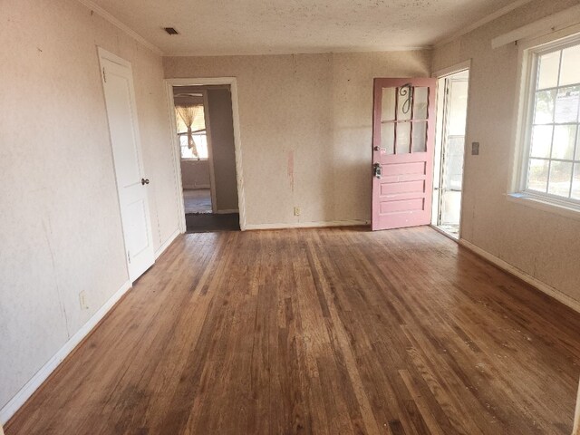 empty room featuring ornamental molding, a textured ceiling, plenty of natural light, and dark wood-type flooring