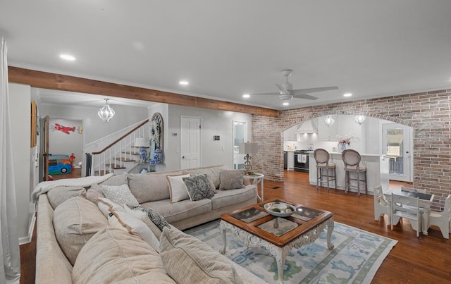 living room with ceiling fan with notable chandelier, dark hardwood / wood-style flooring, and brick wall