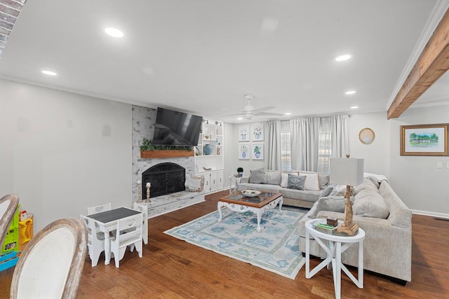 living room featuring dark wood-type flooring, crown molding, ceiling fan, beam ceiling, and a large fireplace