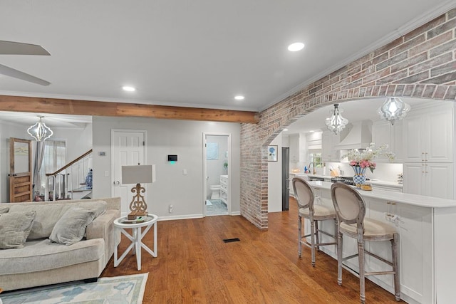 living room with a notable chandelier, light hardwood / wood-style floors, ornamental molding, and brick wall