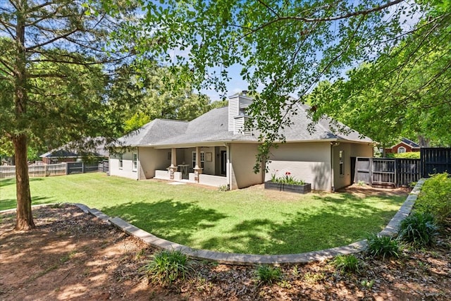 rear view of house with a yard, a chimney, a fenced backyard, and stucco siding
