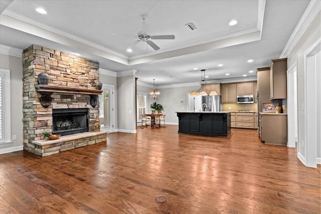 living room featuring dark wood-style flooring, visible vents, ceiling fan with notable chandelier, a fireplace, and a raised ceiling