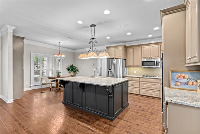kitchen featuring tasteful backsplash, an island with sink, appliances with stainless steel finishes, ornamental molding, and light stone countertops