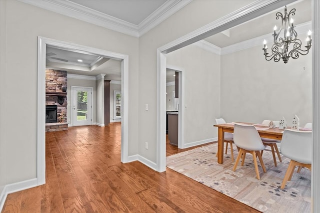 dining room featuring wood finished floors, ornamental molding, a fireplace, baseboards, and a notable chandelier