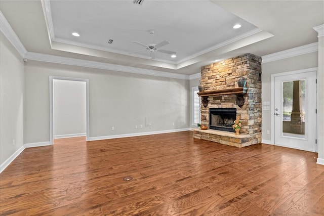 unfurnished living room featuring a tray ceiling, hardwood / wood-style floors, a ceiling fan, and a stone fireplace